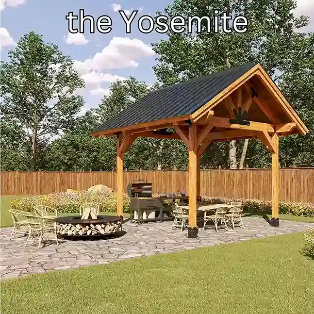 A four-post cedar pavilion with a steep shingled gable roof and an exposed truss, over a stone patio with a dining table and a fire ring on the lawn.