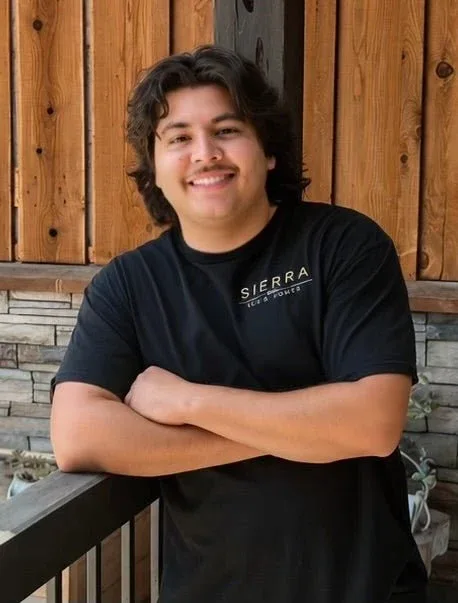 Isaac Meza Jr. in a Sierra shirt, arms folded, on the showroom porch.
