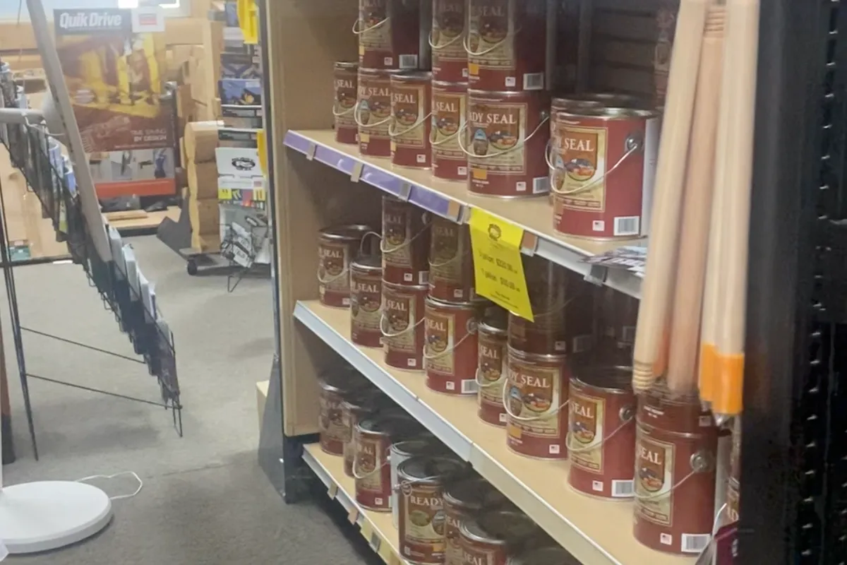 An aisle of Ready Seal stain cans on shelves, with wooden handles racked at the end and a QuikDrive display behind.