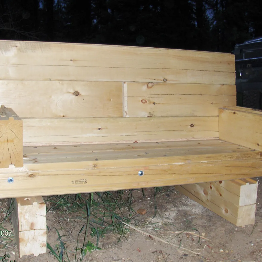 A bench built from D-log offcuts: thick flat-faced cedar boards stacked into the back and the seat, square blocks for legs and arms, photographed at night with a flash.