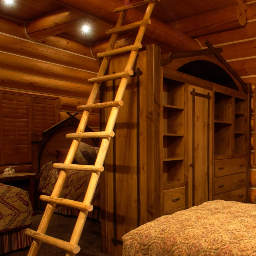 A peeled log ladder, its round rungs set into two log rails, rising past a tall timber armoire to the log beams of the ceiling in a round log bedroom, beds made up below.