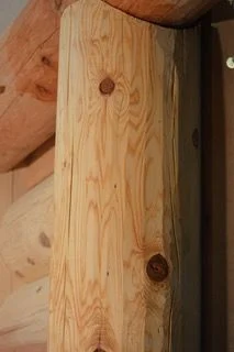The top of a round log post close up, end notched so a flat-faced header sits down into it, the post's grain and knots running up into the joint.