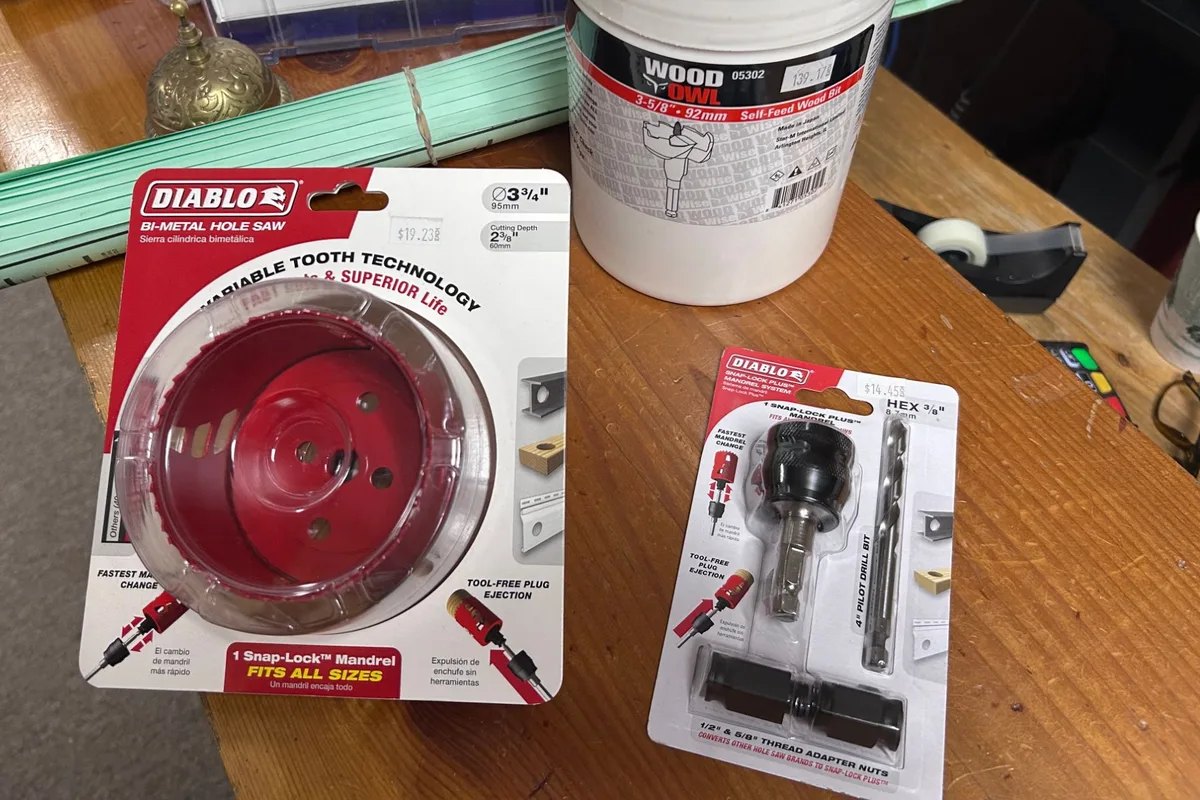 The three pieces of the log rail installation kit on the store counter, still in their packaging: a Diablo 3 3/4 inch bi-metal hole saw in a red and white blister pack, a Wood Owl 3 5/8 inch self-feed wood bit in a white canister, and a Diablo Snap-Lock Plus mandrel with its pilot drill bit and thread adapter nuts, each with a price sticker.