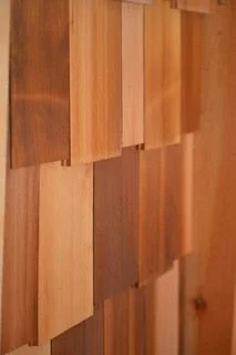 Cedar shingle siding with a staggered butt: shingles of mixed widths and tones, their bottom edges set at uneven heights course after course.