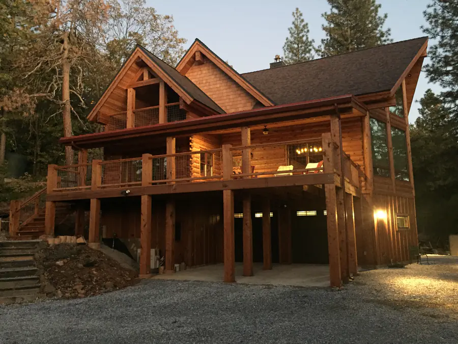 A D-log home at dusk with a deck on log posts, its rounded courses lit from the windows.