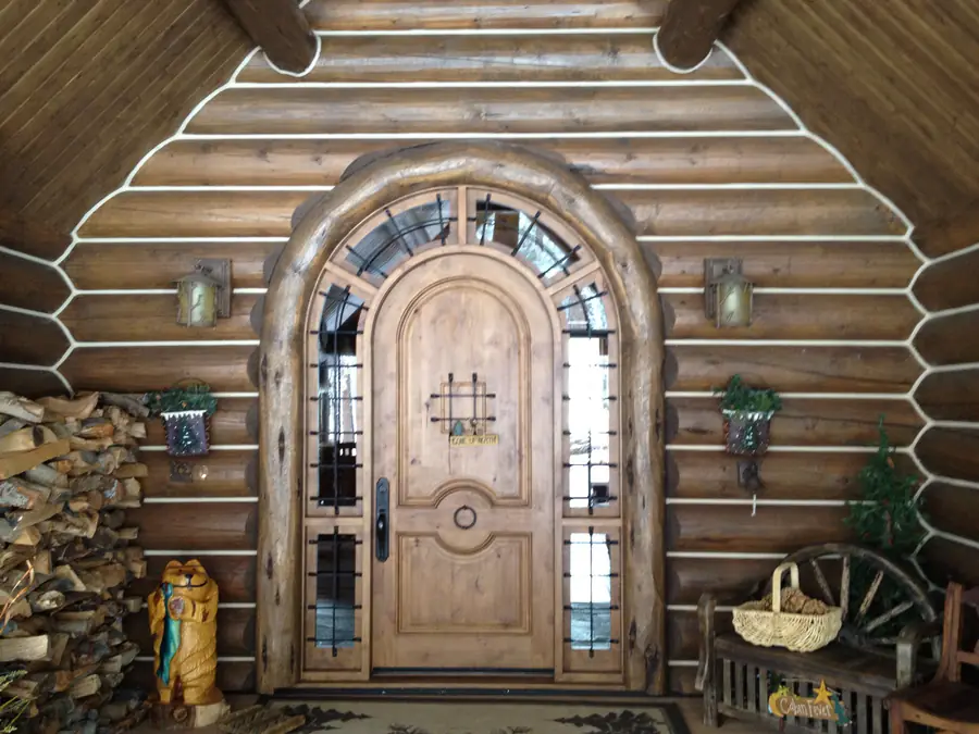 An arched front door set into a round log wall, the logs chinked white between the courses.