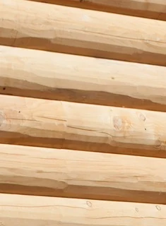 Close on the rounded outside face of a D-log wall, unstained: pale peeled logs with the draw knife's long shallow facets running along each course, a few small knots, and a darker line where each log sits on the next.