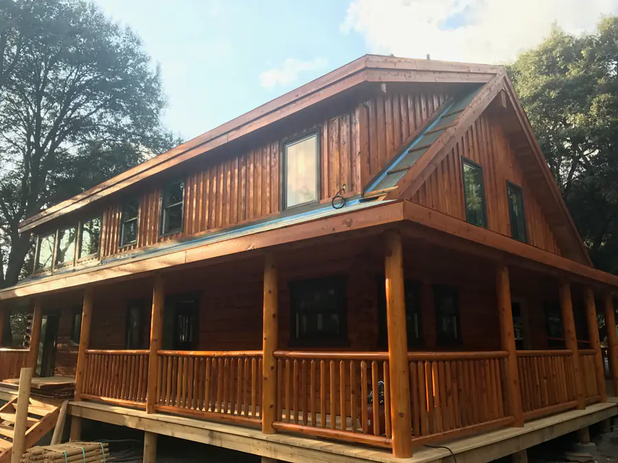A squared timber home with a wraparound porch and a shed dormer, the hewn courses catching the afternoon light.