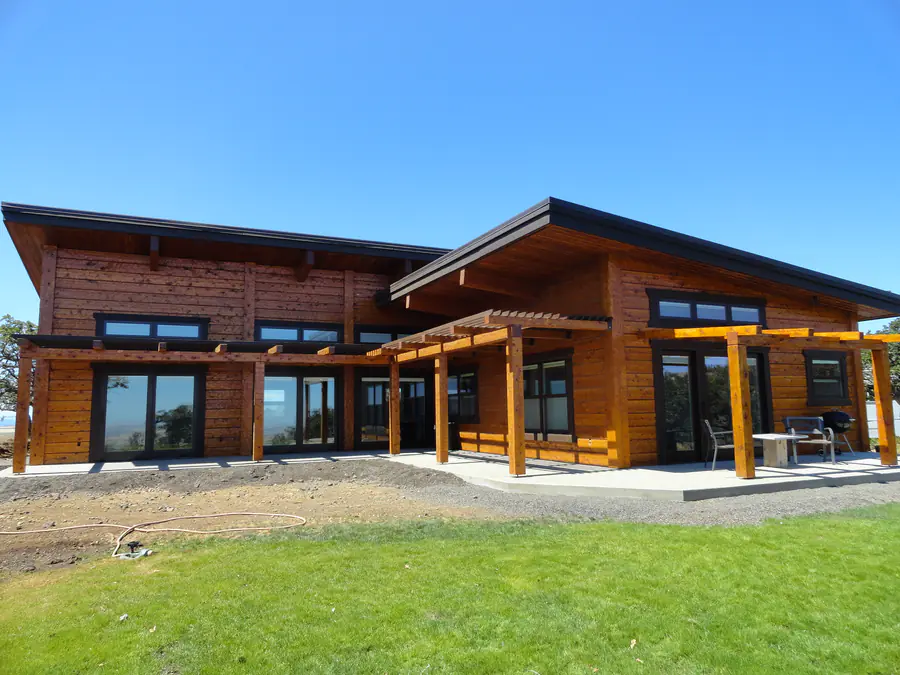 A single-storey squared timber home with a low-pitched roof, wide eaves and a covered patio, on a new lawn.