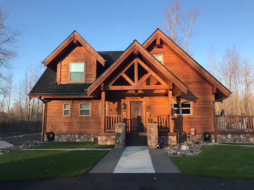 A finished squared timber home with a stone base, a timber-trussed entry gable and a covered porch.