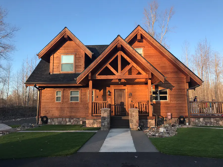 A finished squared timber home with a stone base, a timber-trussed entry gable and a covered porch.