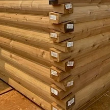 A dovetail corner: D-logs interlocking where two walls meet, each rounded on its face and flat on top, the splayed ends stepping past each other and tagged with their numbers.