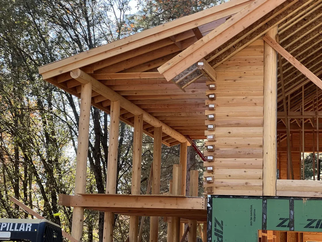 A covered porch under a log gable, rafters and purlins exposed overhead and labeled log ends stepping up the corner.