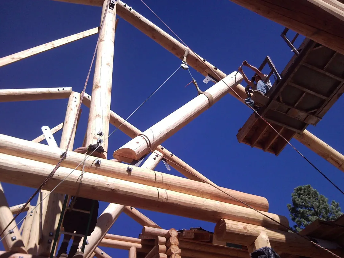 Log roof trusses being set against a deep blue sky, a man working from a raised lift platform.