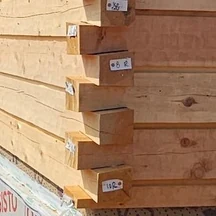 A dovetail corner: squared cedar timbers interlocking where two walls meet, the splayed ends stepping past each other, the hewn faces tagged with their numbers.